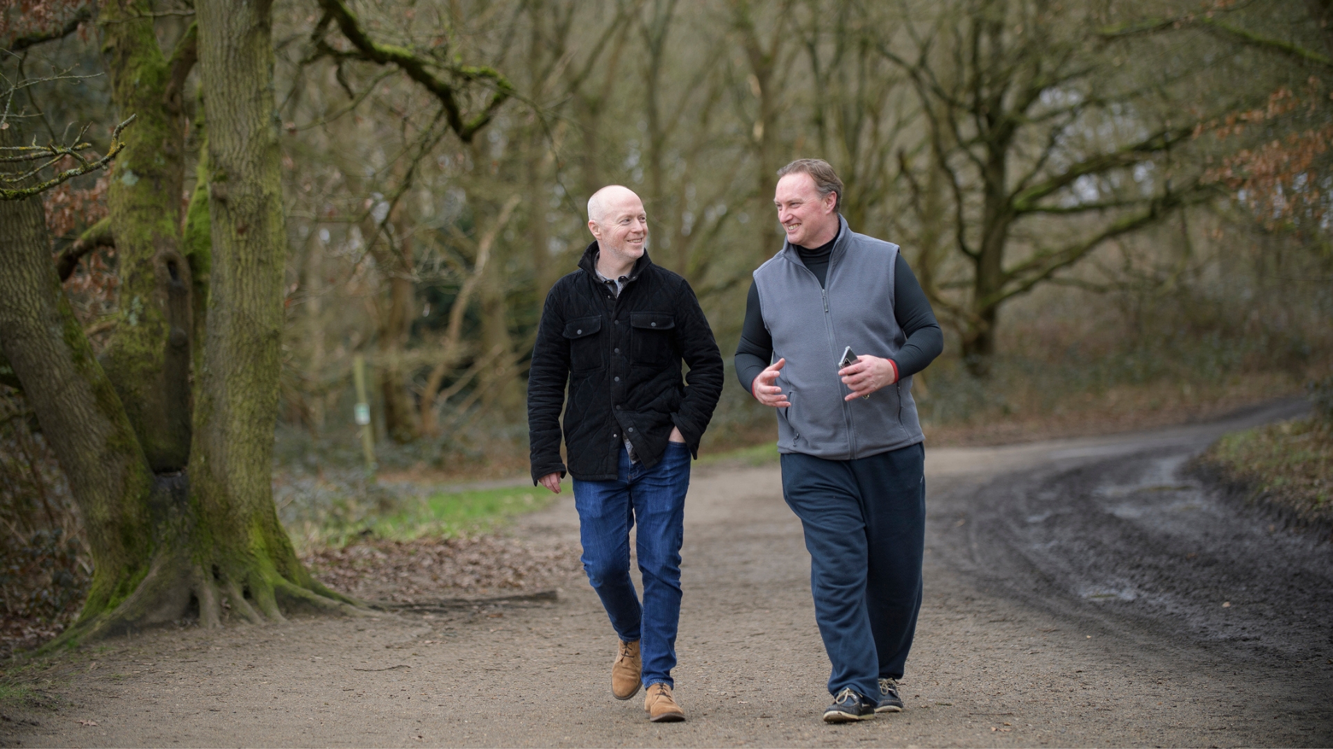 Two people talking while walking along a woodland path.