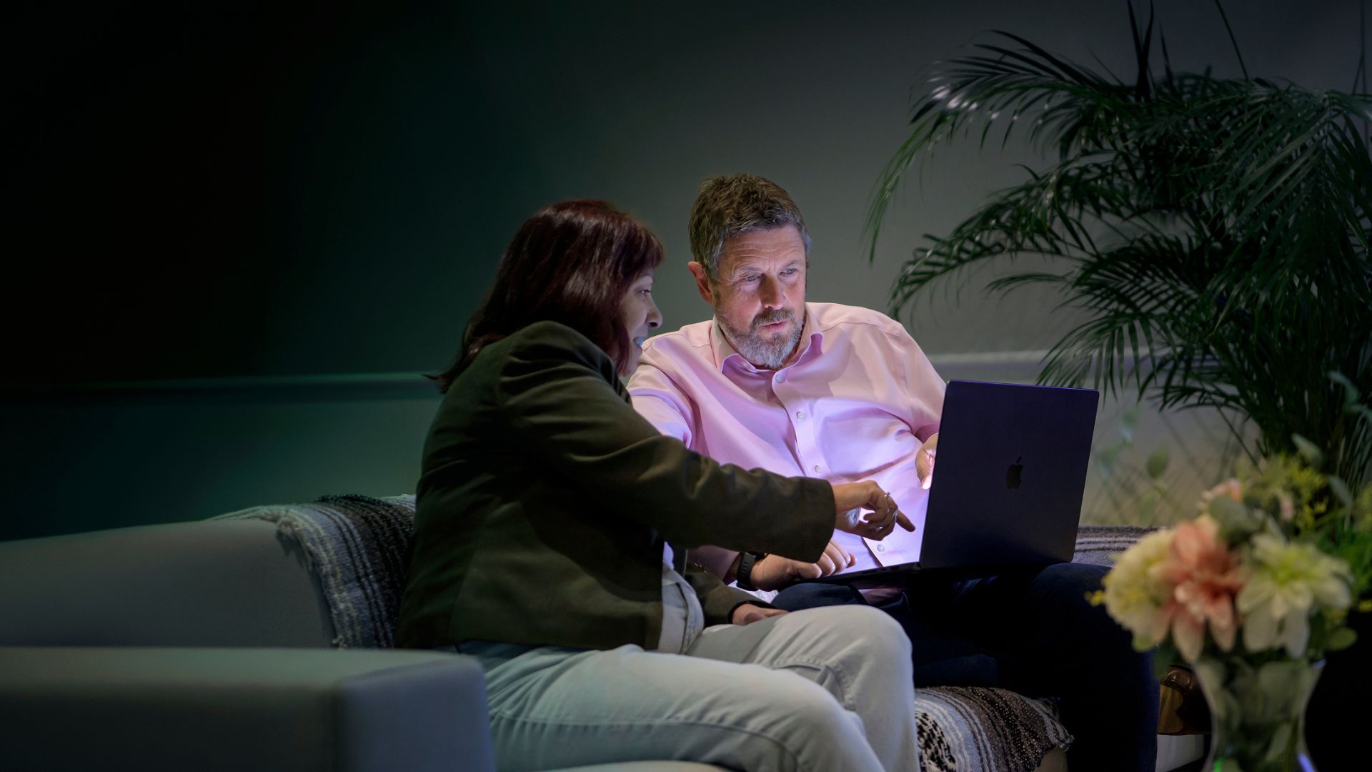 Two adults sitting on a sofa, looking at information on a laptop together
