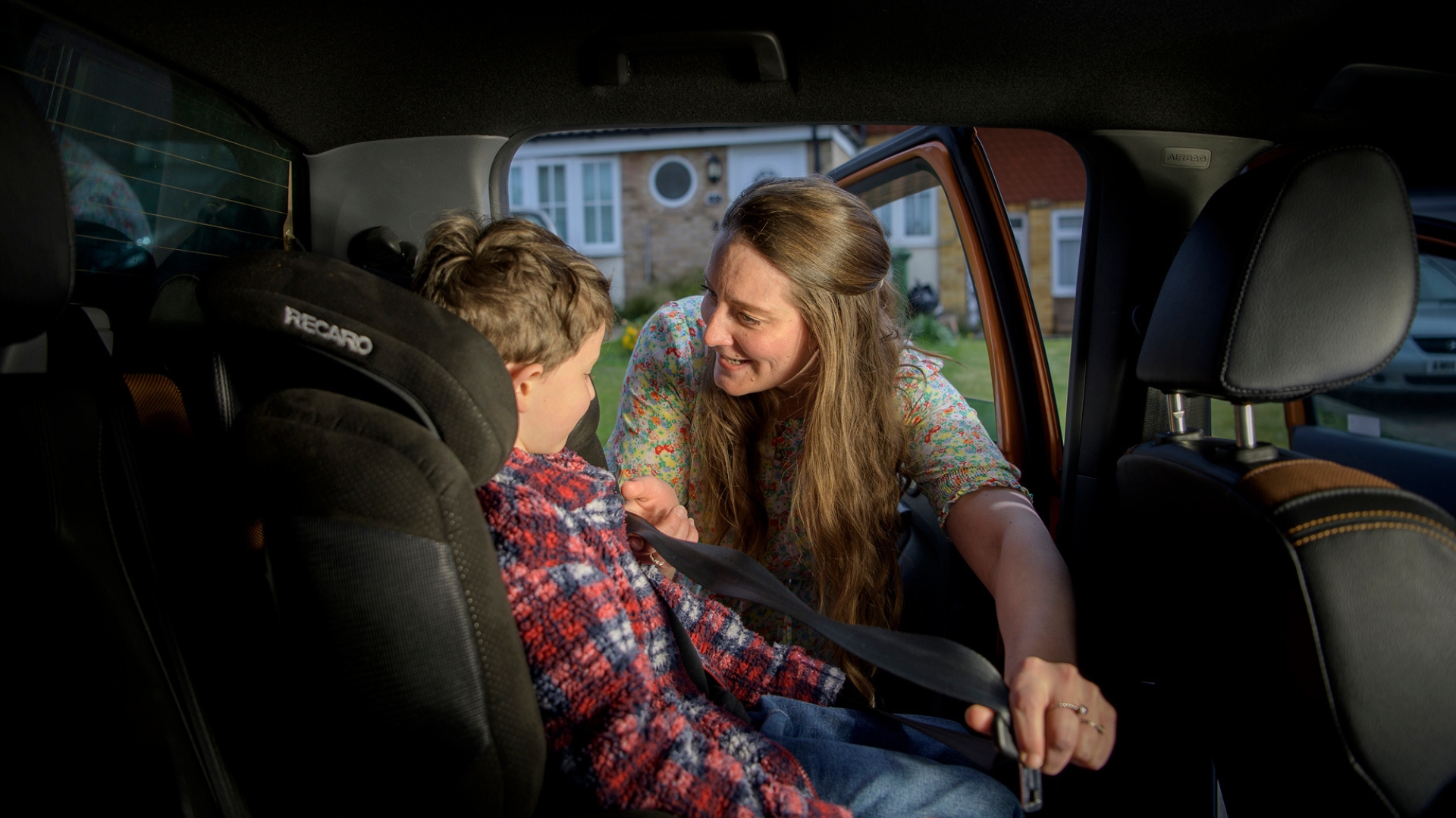An adult securing a child in a car seat with a seatbelt.
