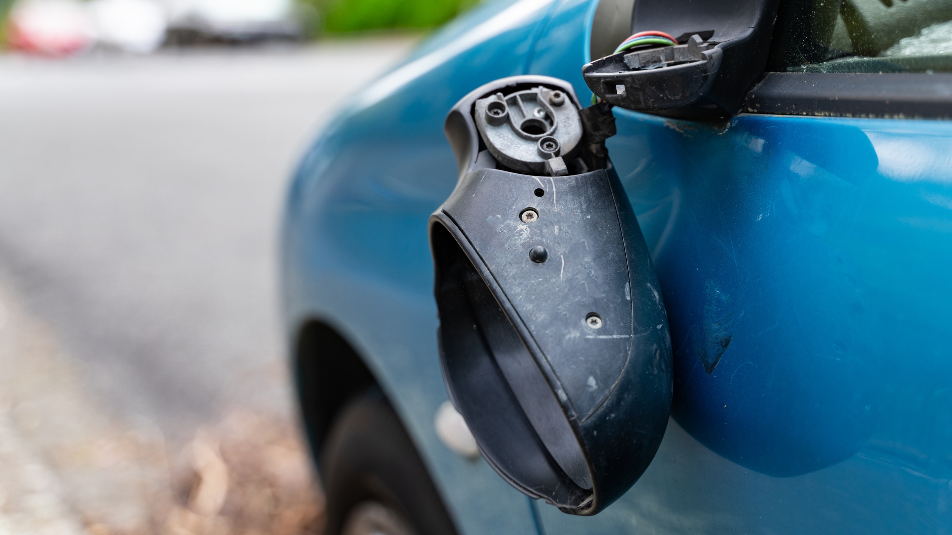 Damaged car wing mirror hanging from the door with exposed wiring.