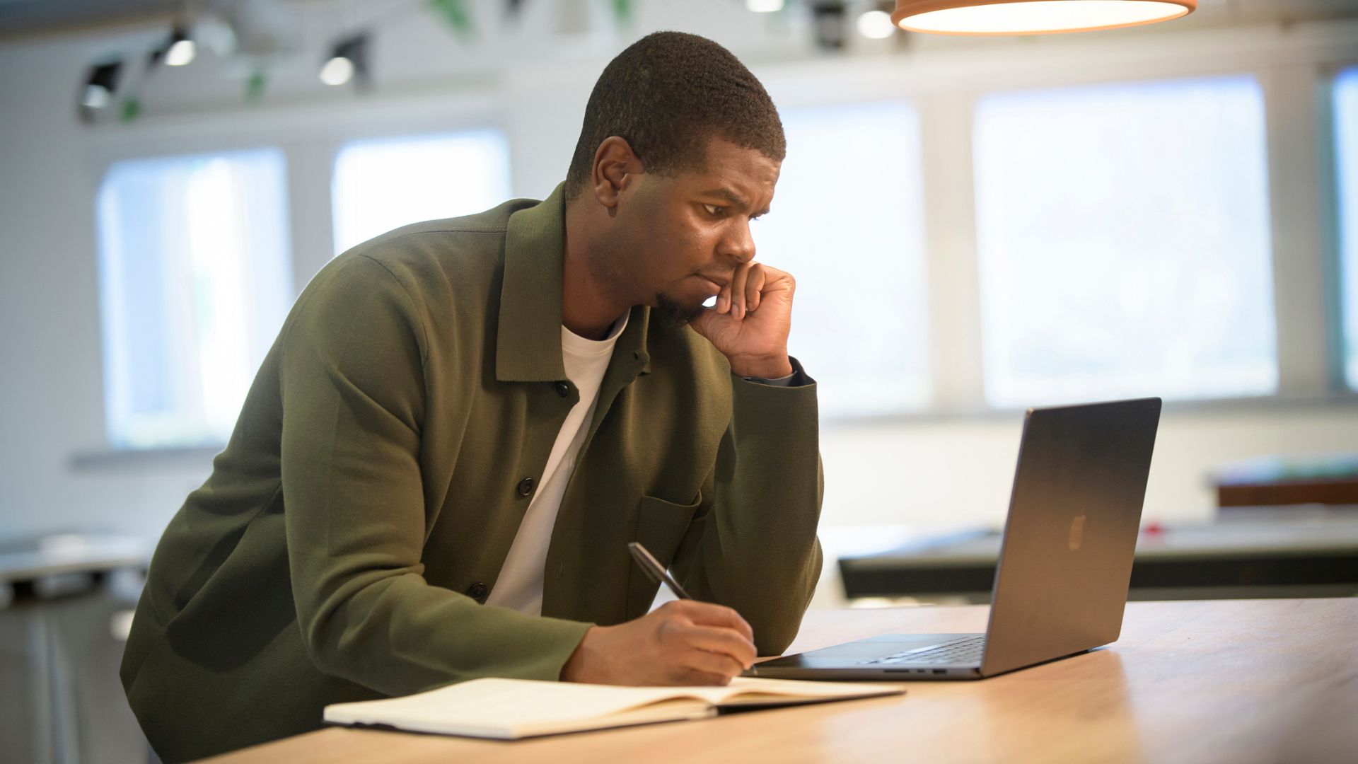 A man looking at a laptop while holding a pen