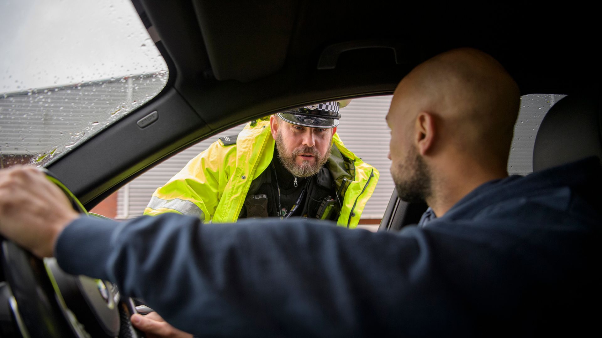 Police officer talks to male driver in car.