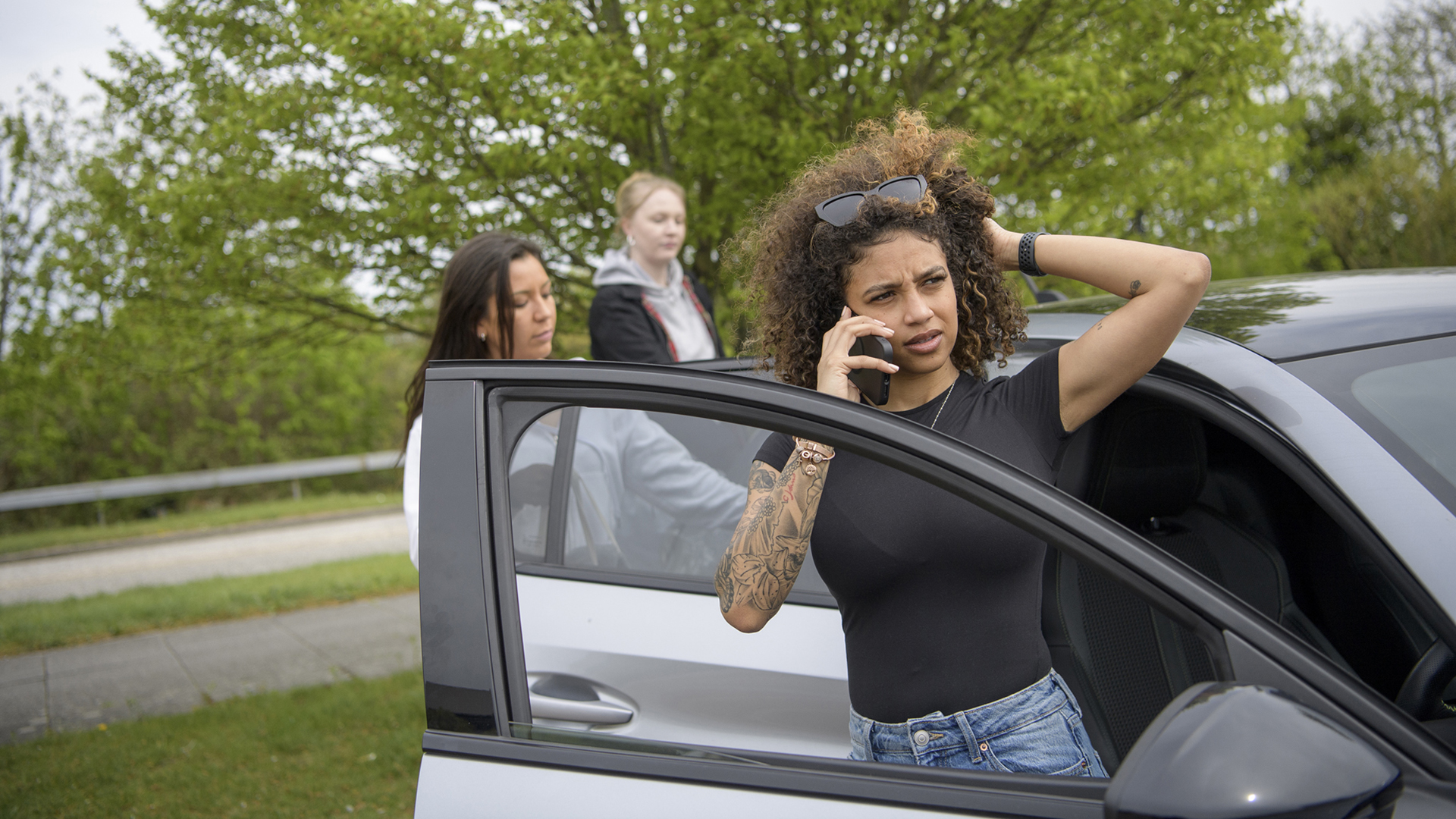 Young woman driver standing next to car on phone looking concerned