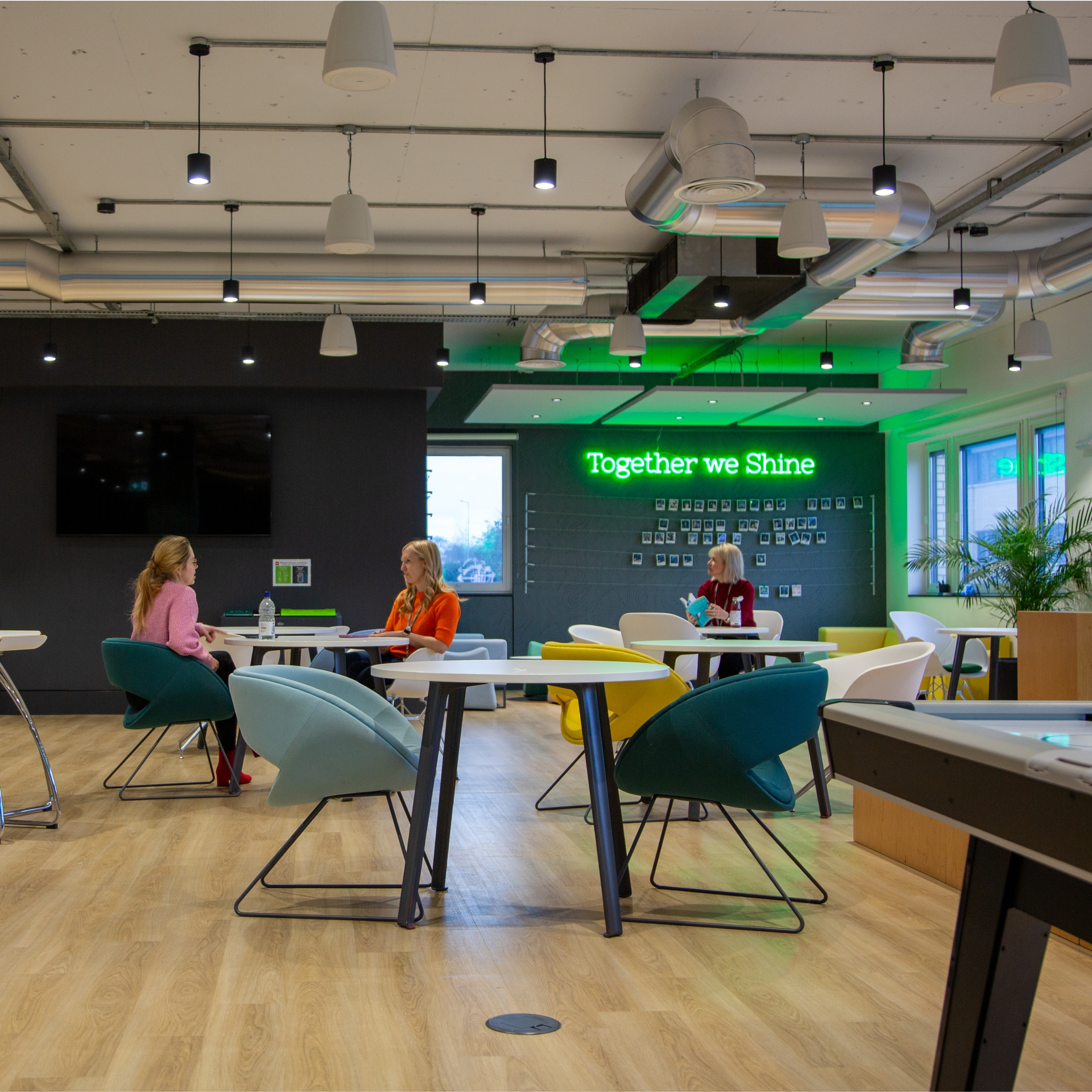 Office breakout area with tables and seating, and a neon sign reading “Together we Shine”.