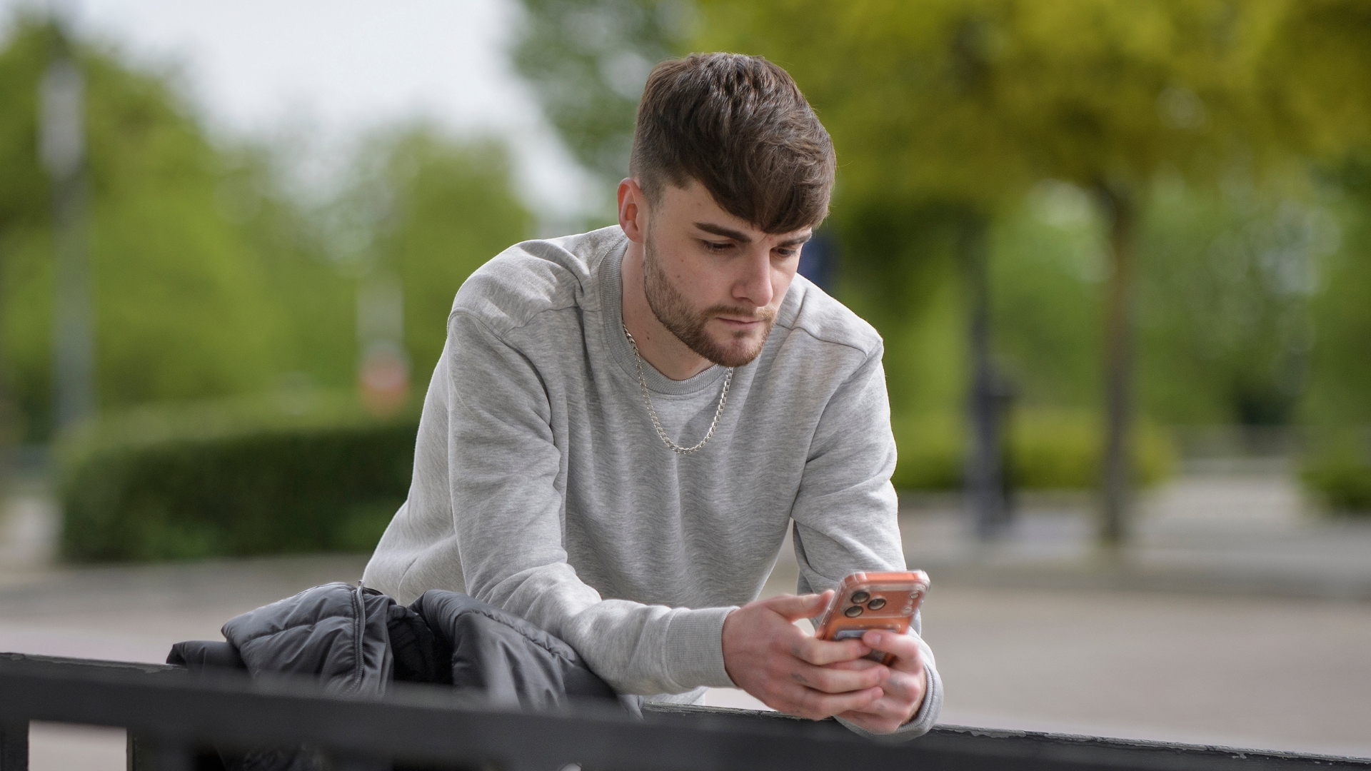 A person leaning on railing outdoors, looking at a mobile phone